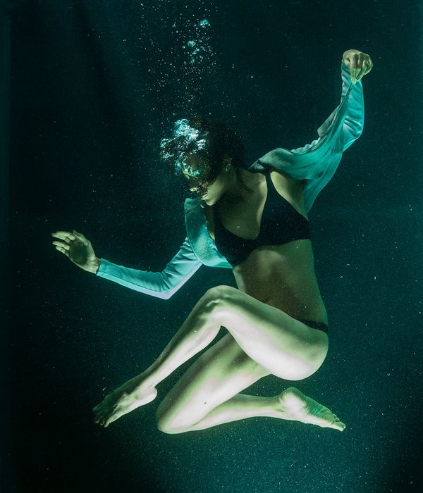 Woman in a dynamic yoga pose against a dark granite background with aqua highlights.